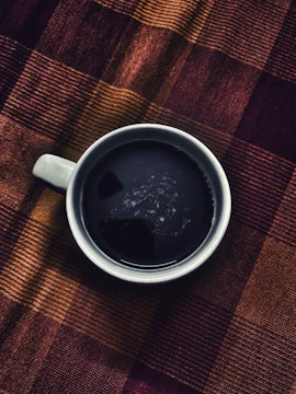 A warm terracotta-hued cup of coffee half-drunk atop textured paper.