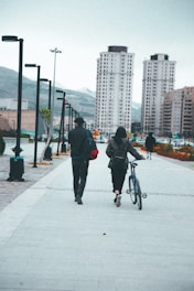 a man and woman walking down a sidewalk with a bicycle