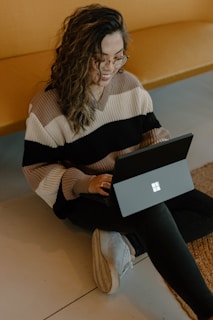 a woman smiling and sitting on the floor with a laptop