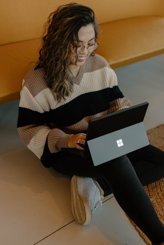 a woman smiling and sitting on the floor with a laptop