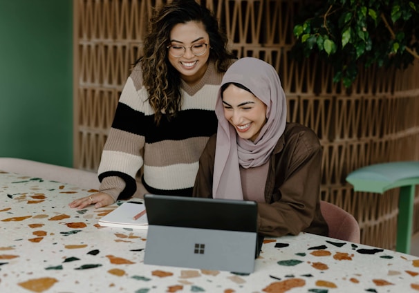 Two women sitting at a table with a laptop