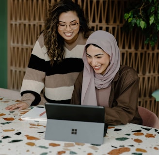 Two women sitting at a table with a laptop