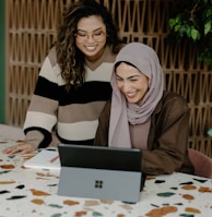 Two women sitting at a table with a laptop