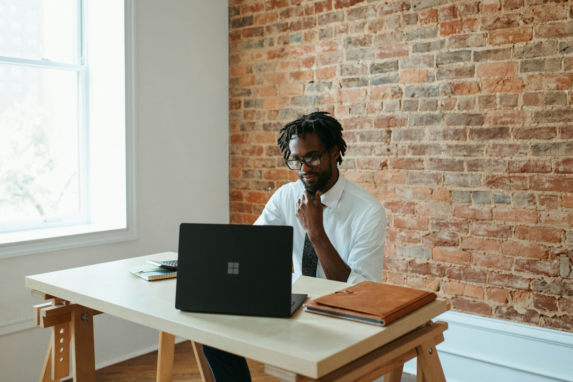 Homme se tenant la barbe assis à un bureau travaillant sur un ordinateur portable Microsoft