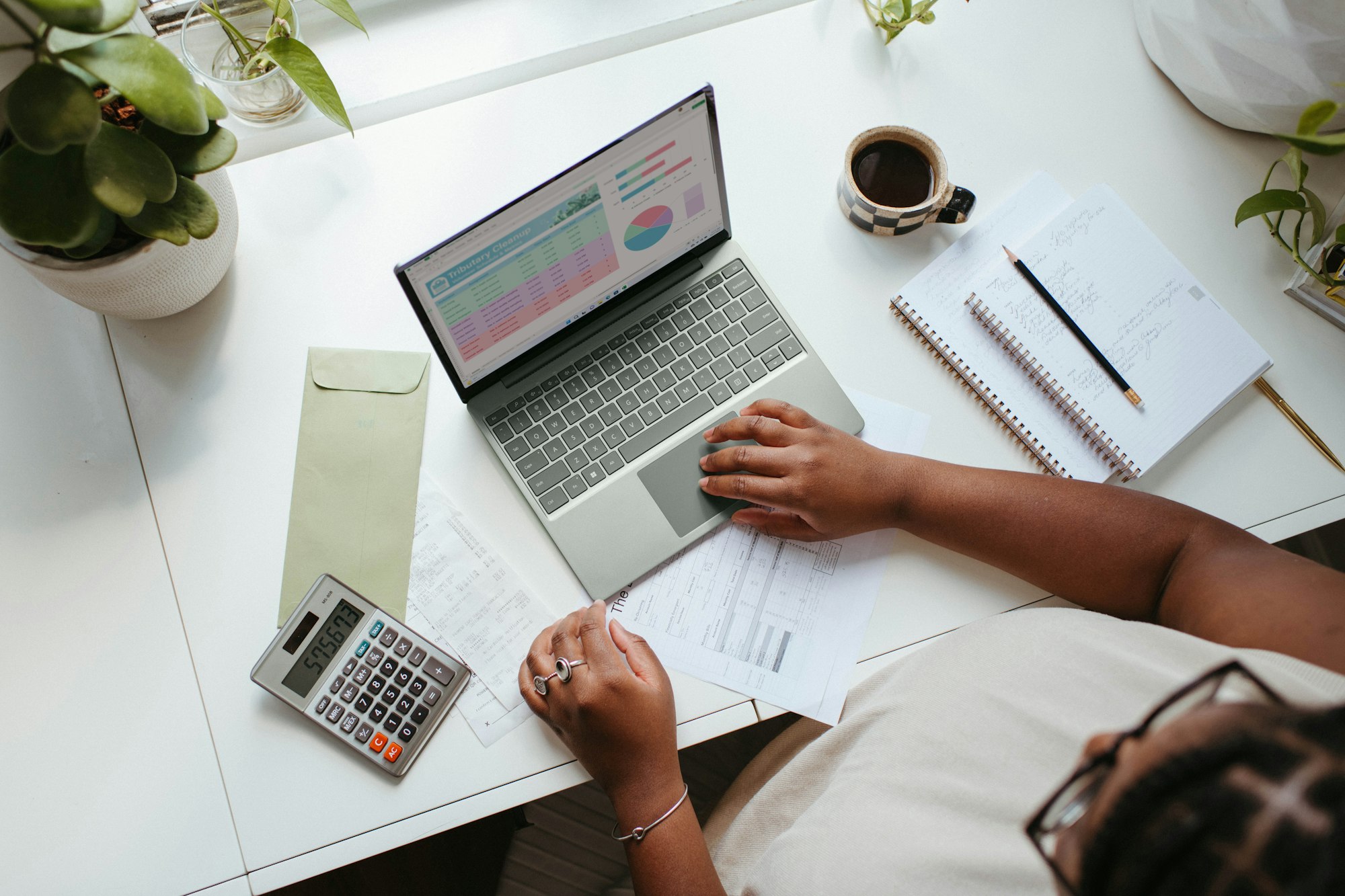 femme travaillant sur un ordinateur avec des documents papiers, des carnets avec des stylos et une calculatrice