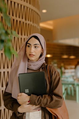 A warm, inviting workspace with a laptop, a purple hijab draped over a chair, and soft natural light.