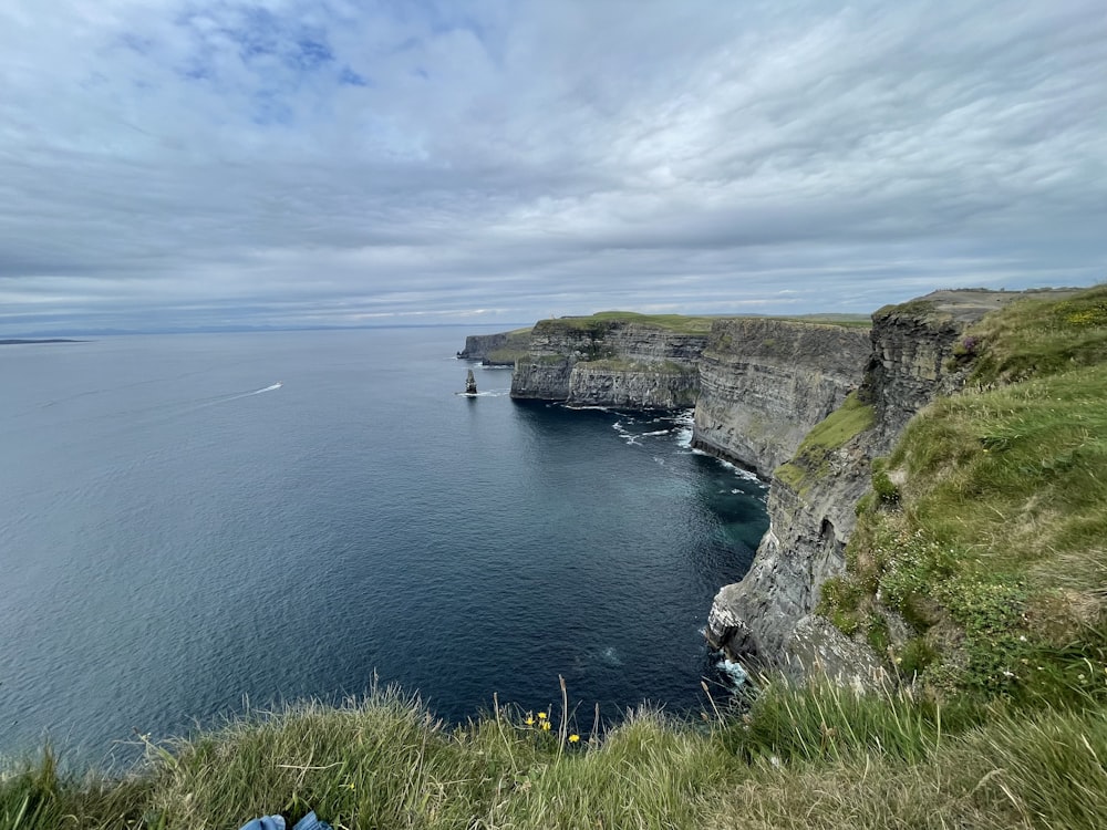 a cliff side with a body of water below with Cliffs of Moher in the background