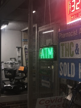 The scene depicts a store window at night with a green ATM sign. Inside, there's a black mobility scooter covered with transparent plastic and marked with a price tag. Surrounding signage includes references to THC, COVID-19 tests, and a lottery jackpot display.