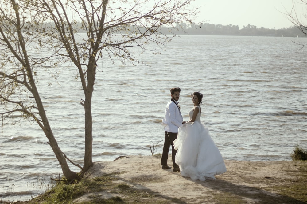 a man and woman in wedding attire standing on a beach by water