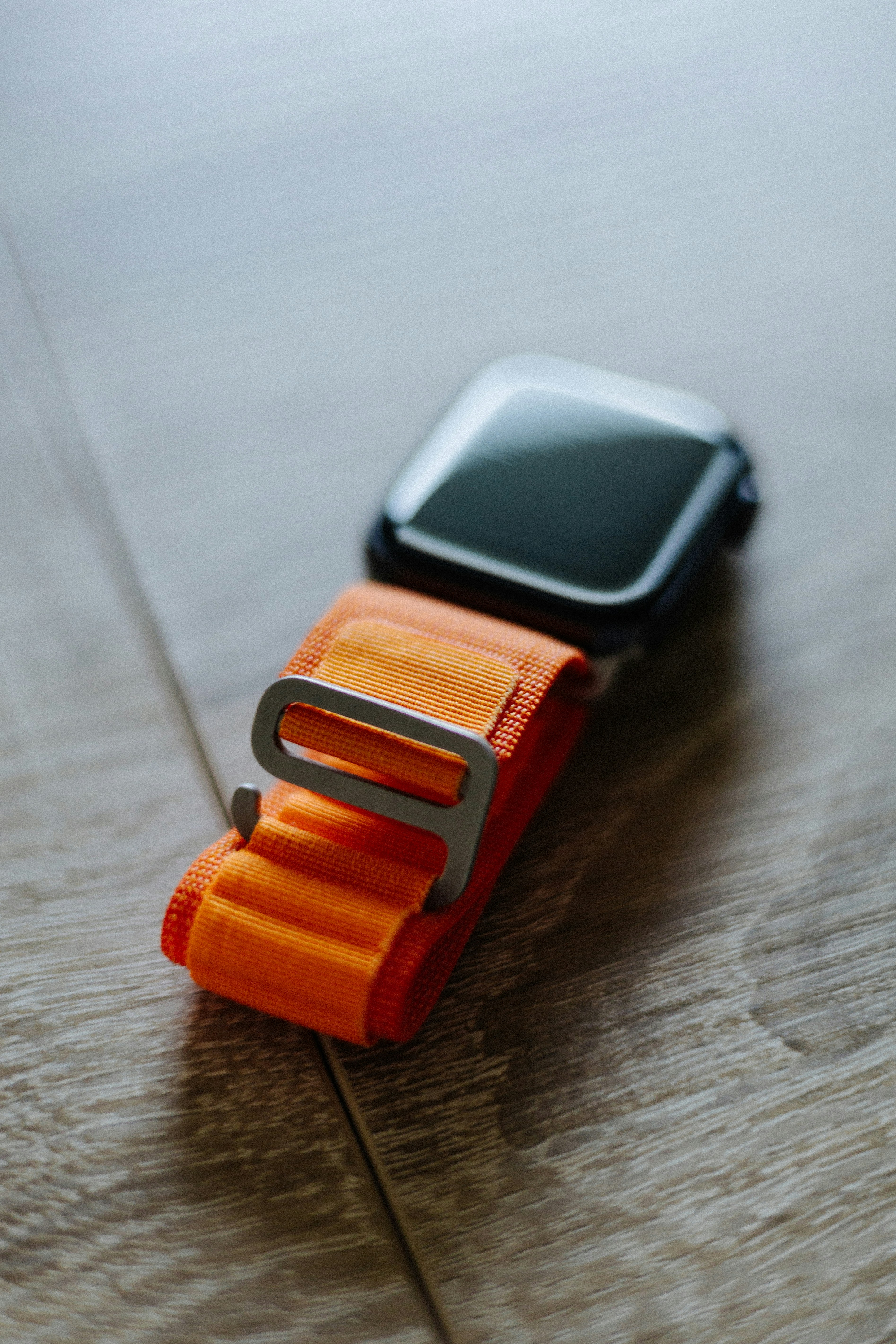 Titanium smartwatch with orange band on dark surface, premium wearable technology