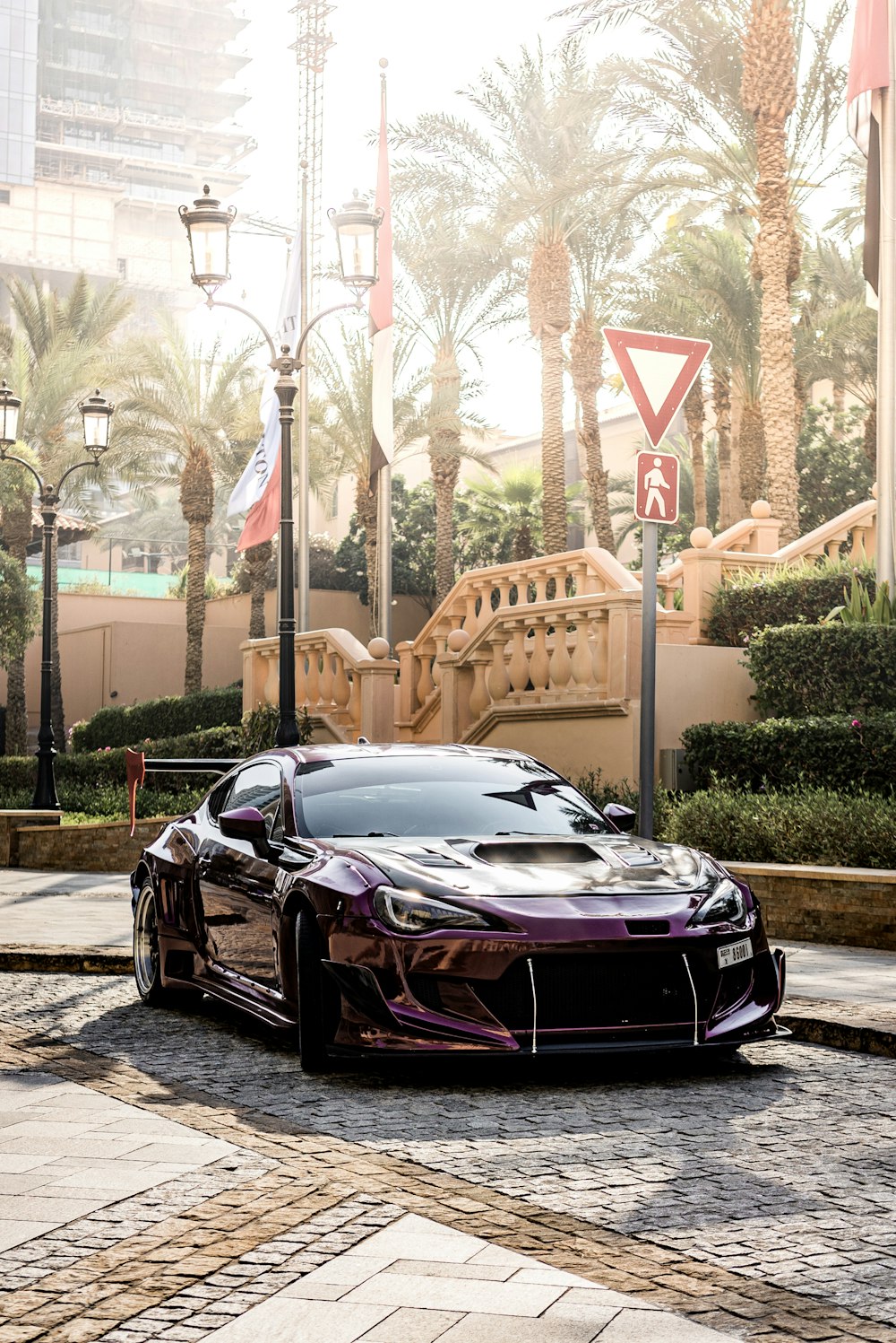 a black sports car parked on a brick road with trees and a bridge