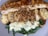 A plate featuring slices of grilled chicken breast topped with a rich brown sauce. Accompanying the chicken are slices of seasoned roasted potatoes and crispy fried onions. Beneath lies a bed of sautéed spinach mixed with melted white cheese, creating a creamy texture.