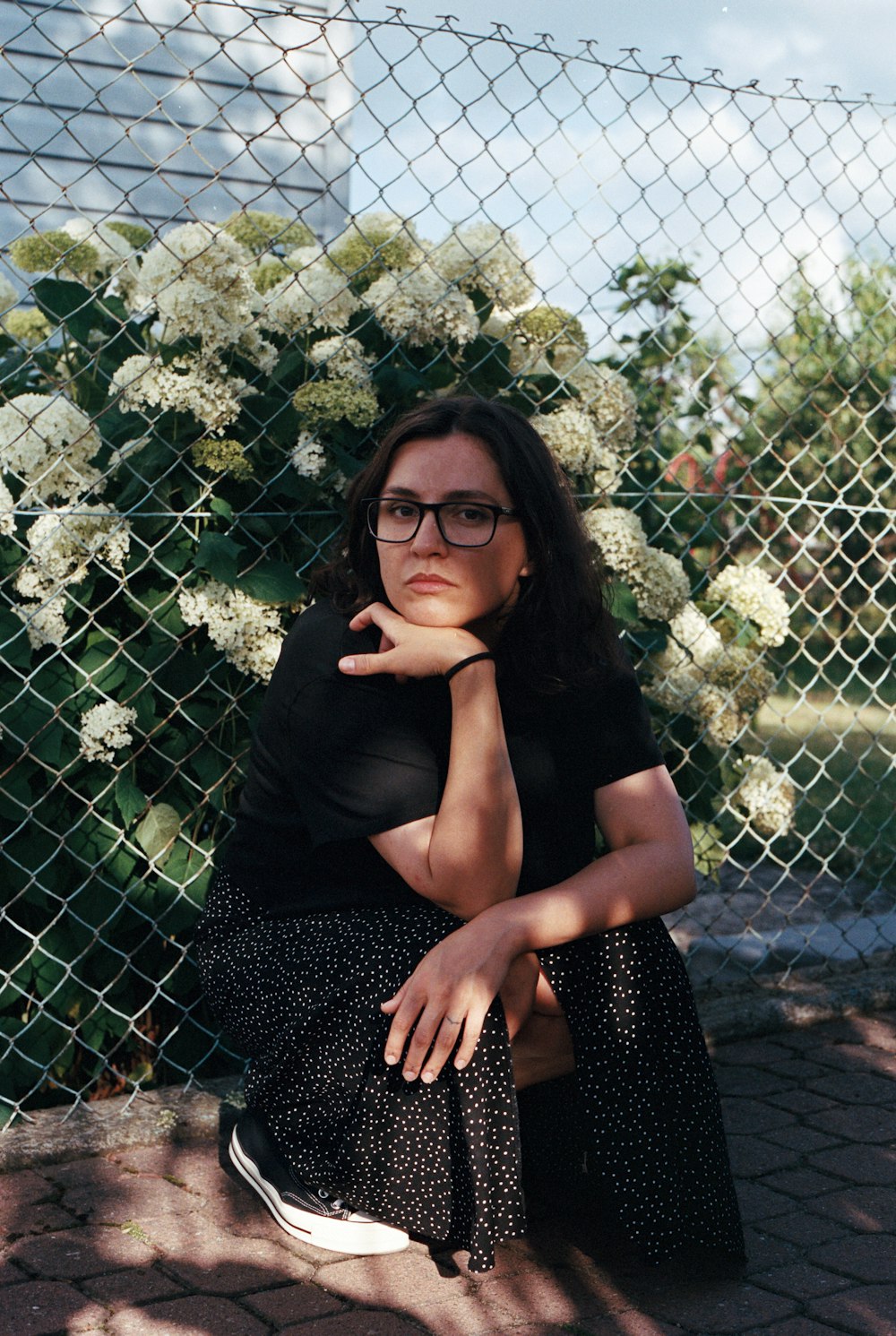 a woman sitting on a stone ledge with a fence and flowers behind her