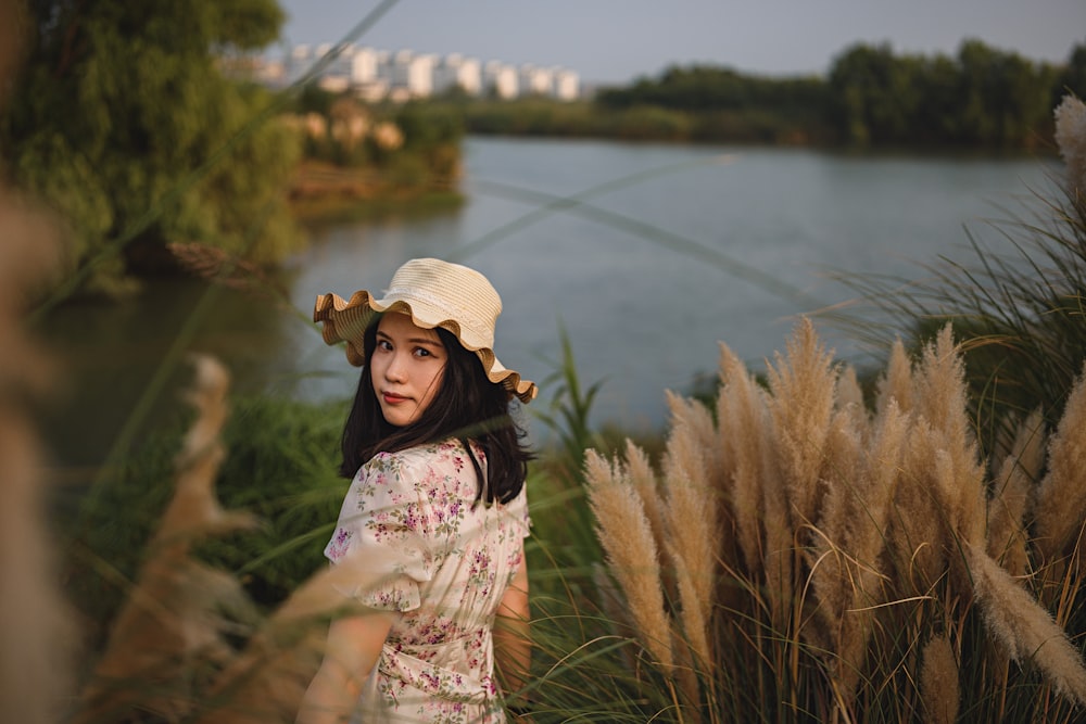 a person in a hat standing in tall grass by a body of water