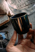 A terracotta ceramic cup on a cream ivory linen cloth beside a notebook with handwritten notes about the collections