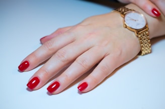 a woman's hand with red fingernails and a gold watch
