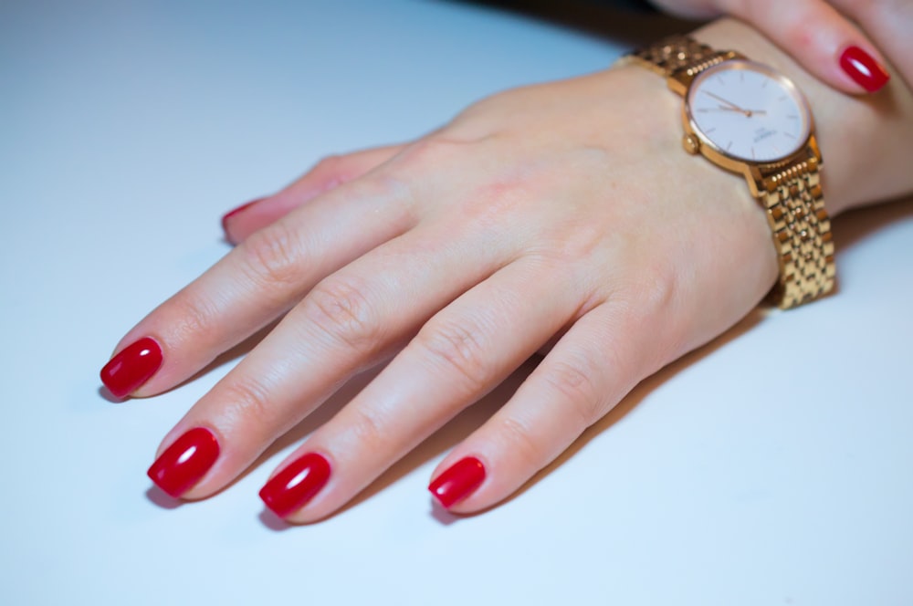 a woman's hand with red fingernails and a gold watch