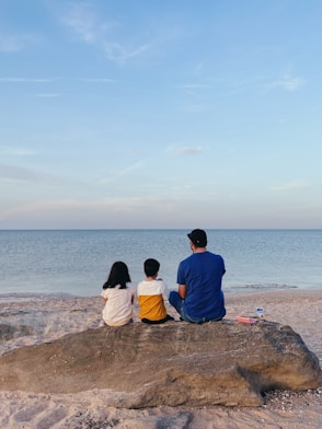 a man and a couple of children sitting on a rock looking at the water