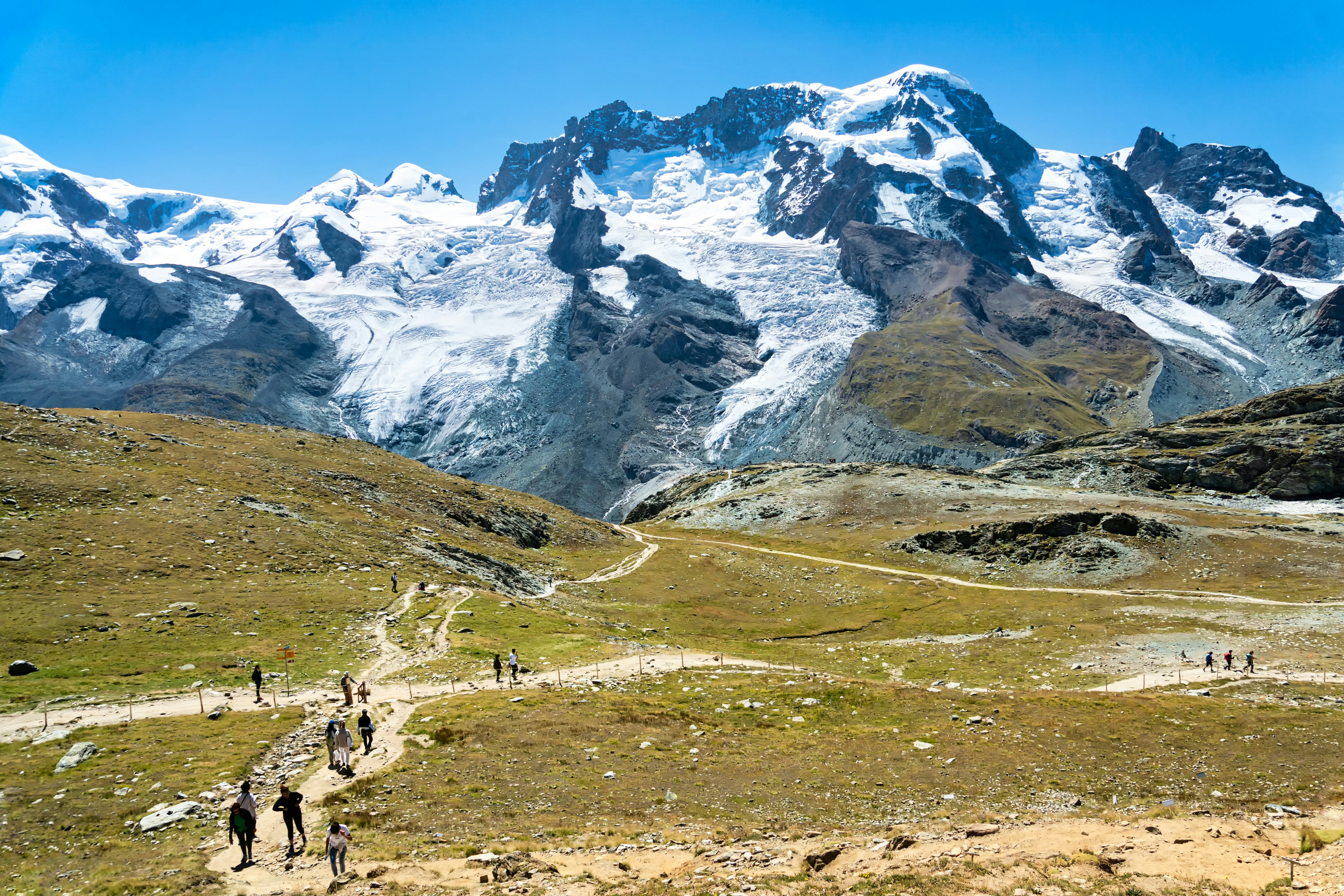 a group of people walking on a trail in front of snowy mountains