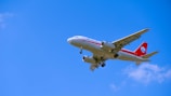 A commercial airplane in flight is captured against a clear blue sky, featuring a white fuselage with red accents and a red tail displaying a logo.