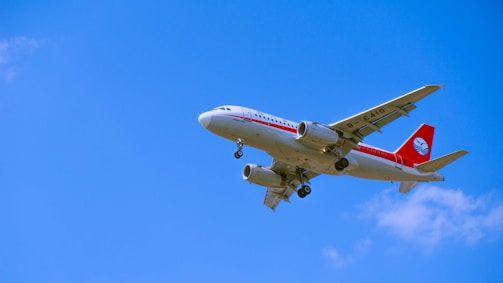 A commercial airplane in flight is captured against a clear blue sky, featuring a white fuselage with red accents and a red tail displaying a logo.