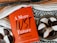 A red book titled "A More Just Future" by Dolly Chugh is placed next to a plate of black and white cookies. The book has text describing it as a tool for psychological and social change. The background includes a striped woven fabric in earthy tones.