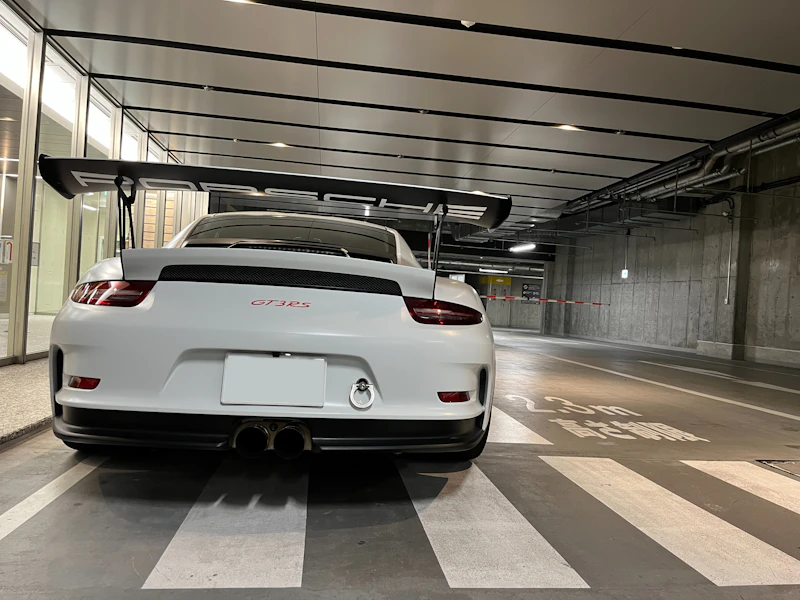 A white low sports car with a tall rear wing, seen from behind in a garage