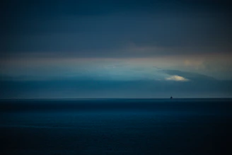 A mysterious, dark ocean horizon under a stormy sky, with faint outlines of distant, shadowy sails barely visible.
