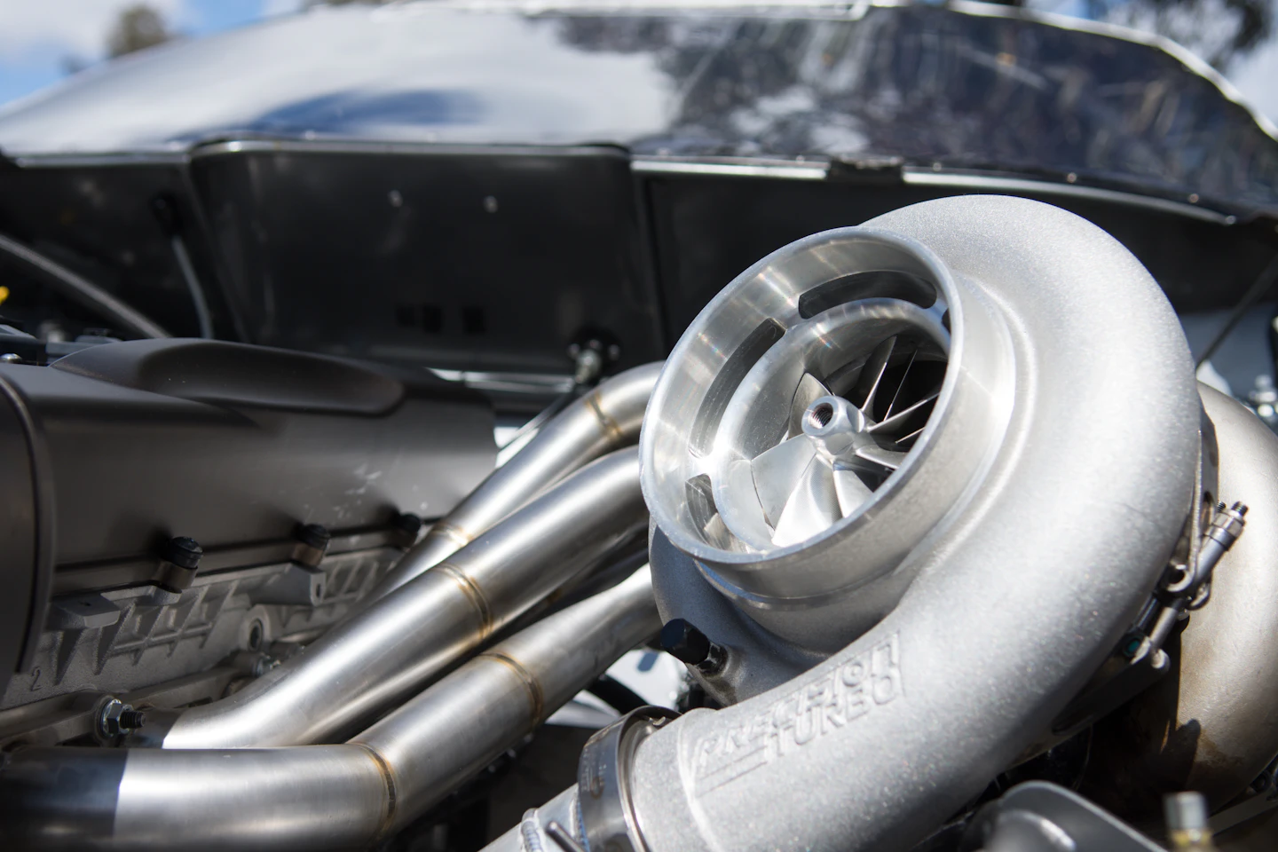 A polished turbocharger compressor housing mounted on an engine, exhaust piping visible
