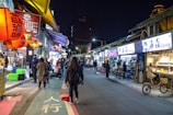 A bustling street market in Bangkok glowing with colorful lanterns at dusk.