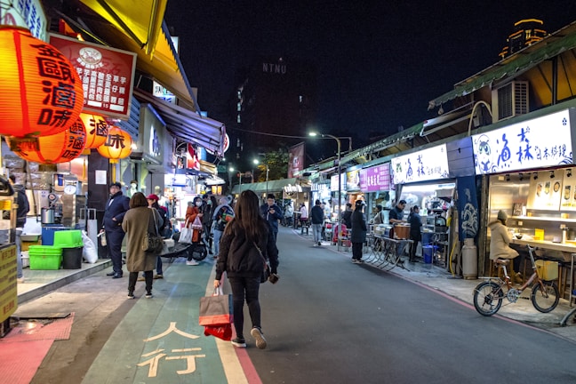 A bustling street market in Bangkok glowing with colorful lanterns at dusk.