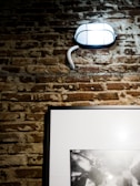 An industrial metal wall sconce mounted on a textured brick wall.