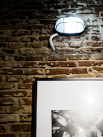 An industrial metal wall sconce with exposed bulbs mounted on a textured brick wall.