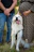 a dog sitting on grass with people standing around