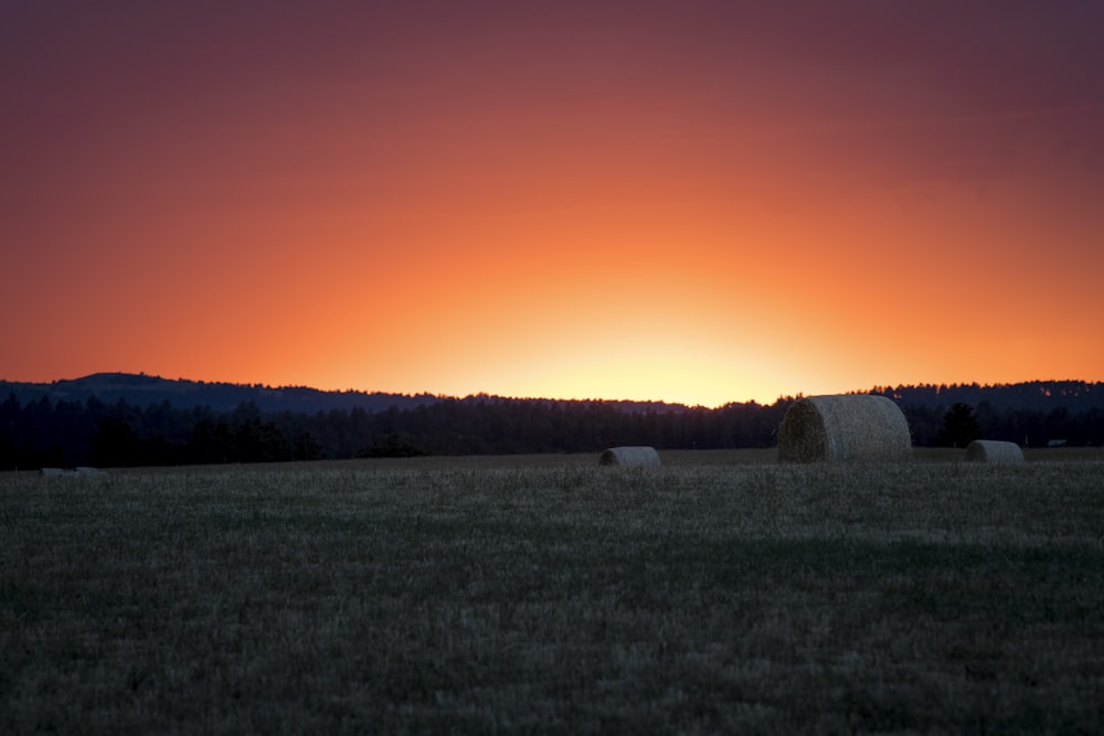 a field with a few bales of hay in it and a sunset in the background