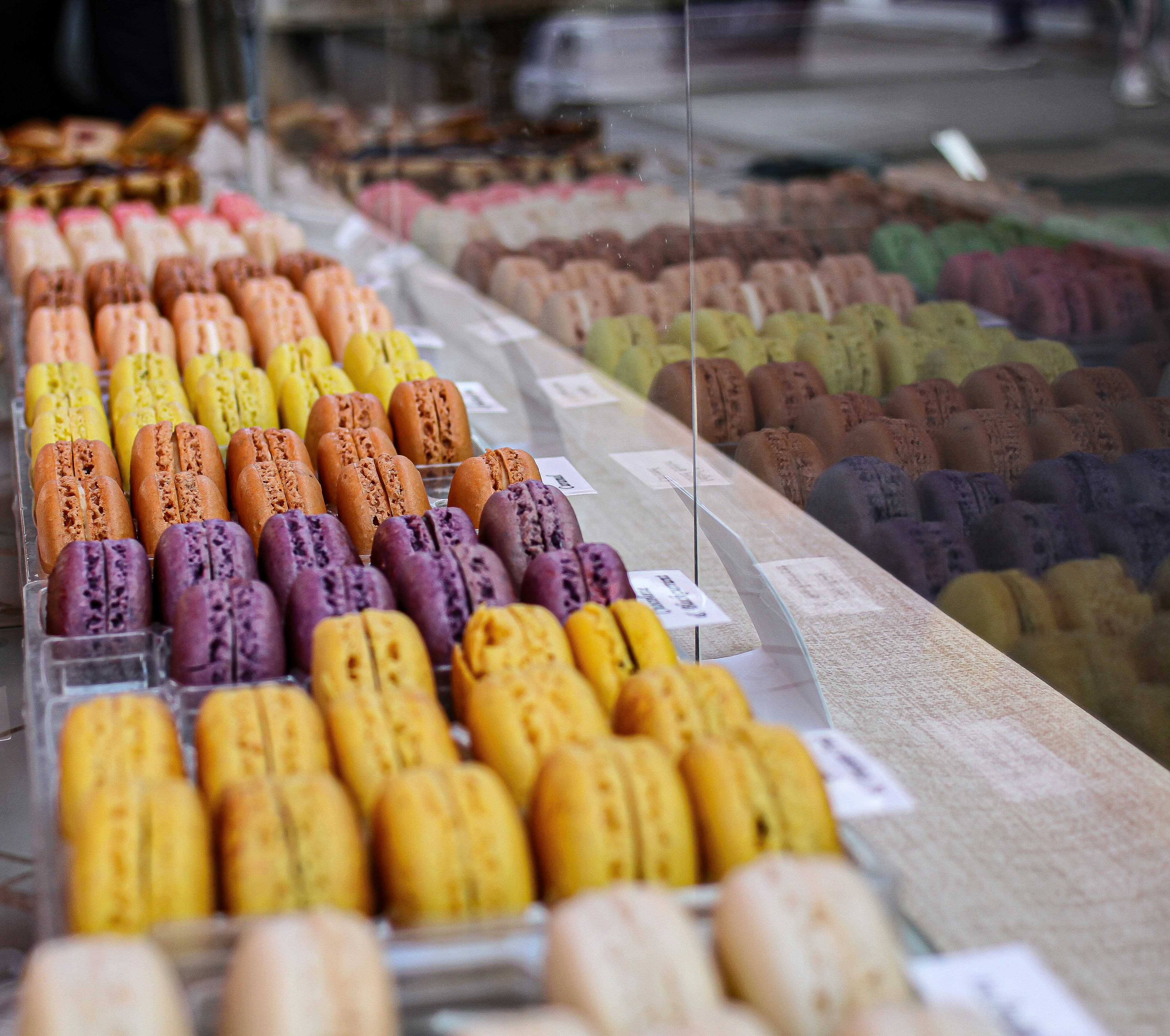 a display of various snacks, Rows of macaron on a counter with a reflection
