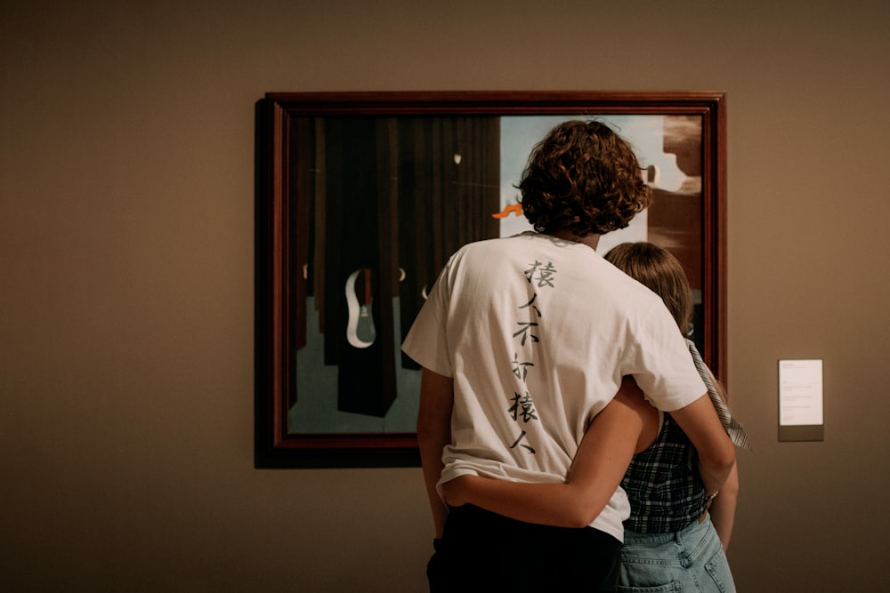 a couple of people looking at a painting on a wall