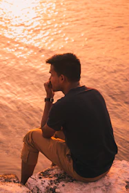 Person reflecting peacefully by the sea during a soft sunset.