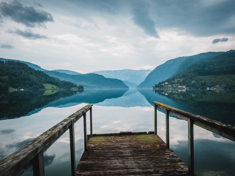 a wooden bridge over a body of water with mountains in the background