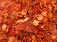 Close-up of crushed red pepper flakes with a hint of green herbs, highlighting texture and color.