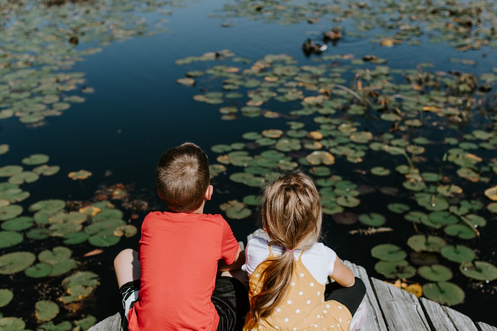 a man and woman sitting on a bench looking at a pond