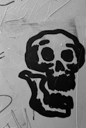 Close-up of a spray-painted surface in black, red, and yellow with small skull patterns floating in the background.