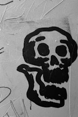 Close-up of a spray-painted wall featuring black, red, and yellow colors with small skulls subtly floating in the background.