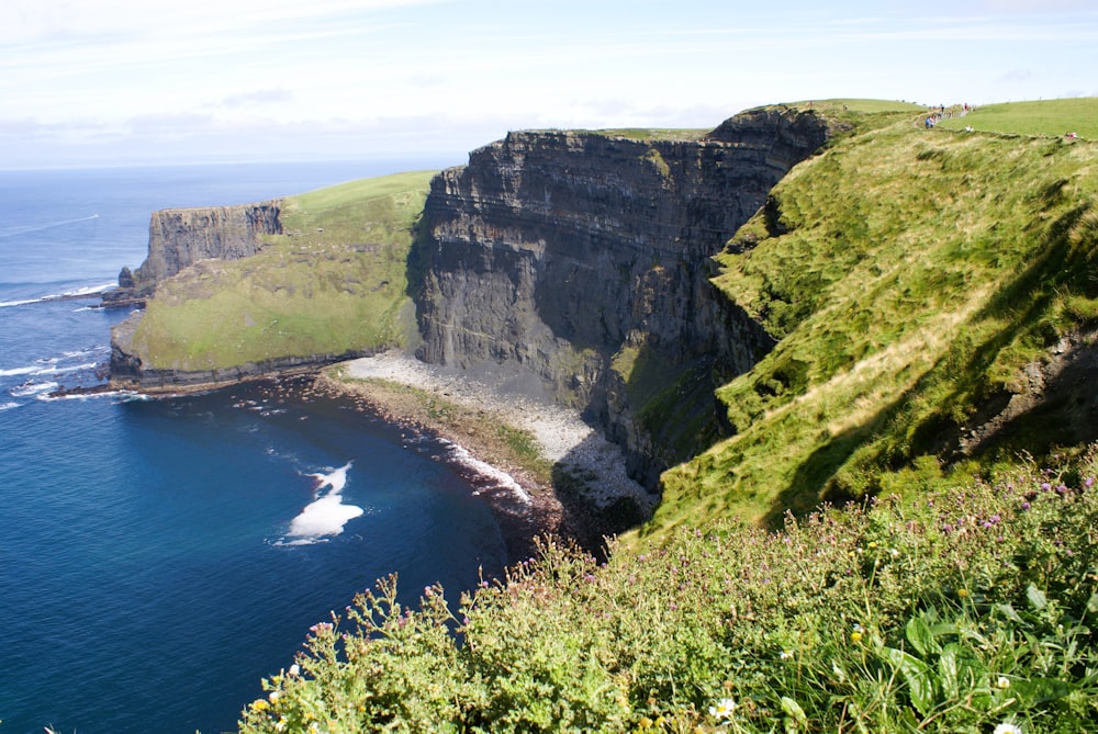a cliff with a body of water below with Cliffs of Moher in the background