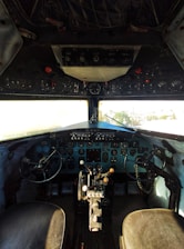 A detailed view of an aircraft cockpit featuring numerous dials, switches, and controls. Two pilot seats are visible with control yokes in front of them. The dashboard is filled with various instruments necessary for flight navigation and management.
