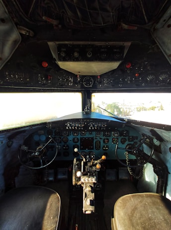 A detailed view of an aircraft cockpit featuring numerous dials, switches, and controls. Two pilot seats are visible with control yokes in front of them. The dashboard is filled with various instruments necessary for flight navigation and management.