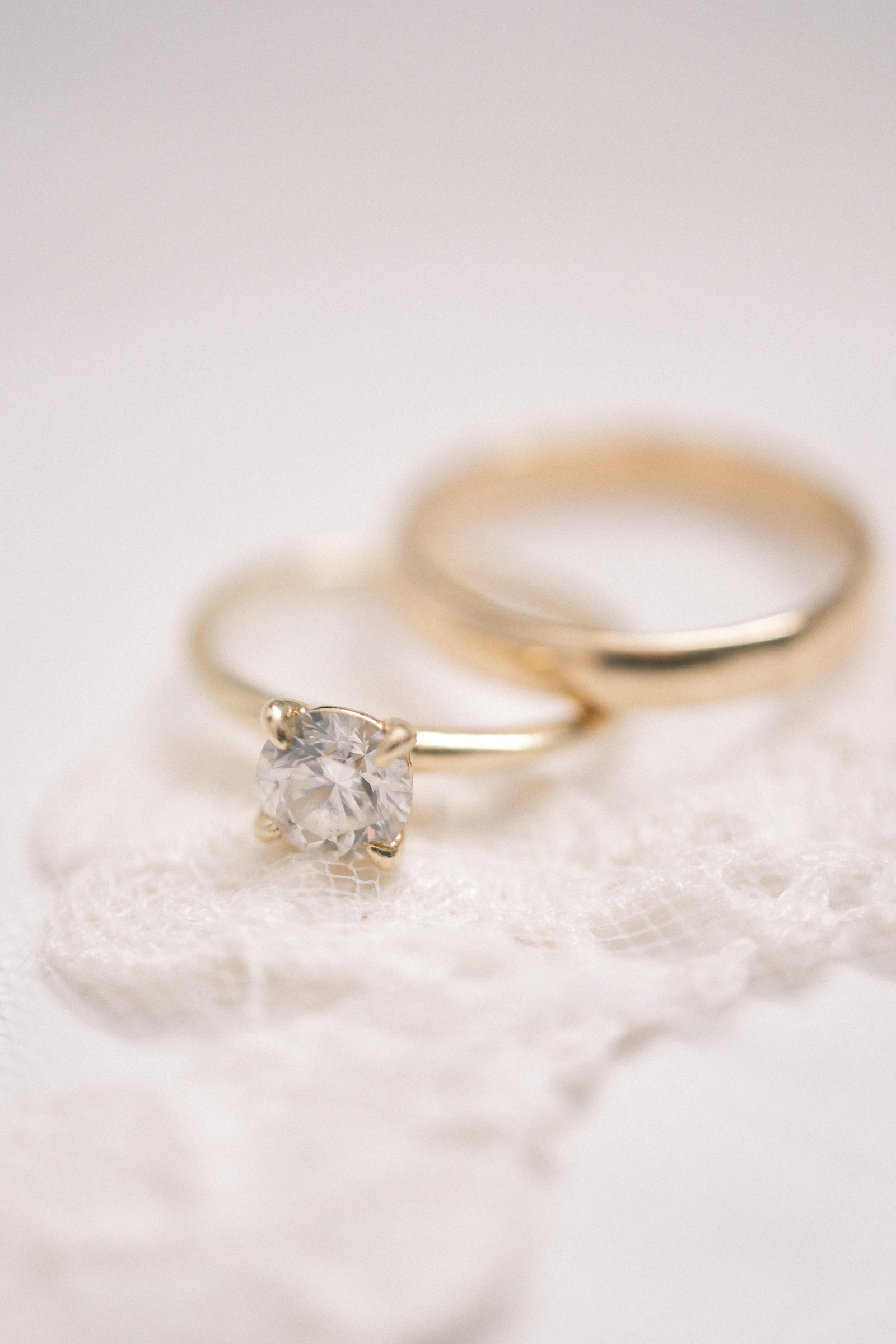 Gold diamond solitaire engagement ring and matching wedding band on soft lace