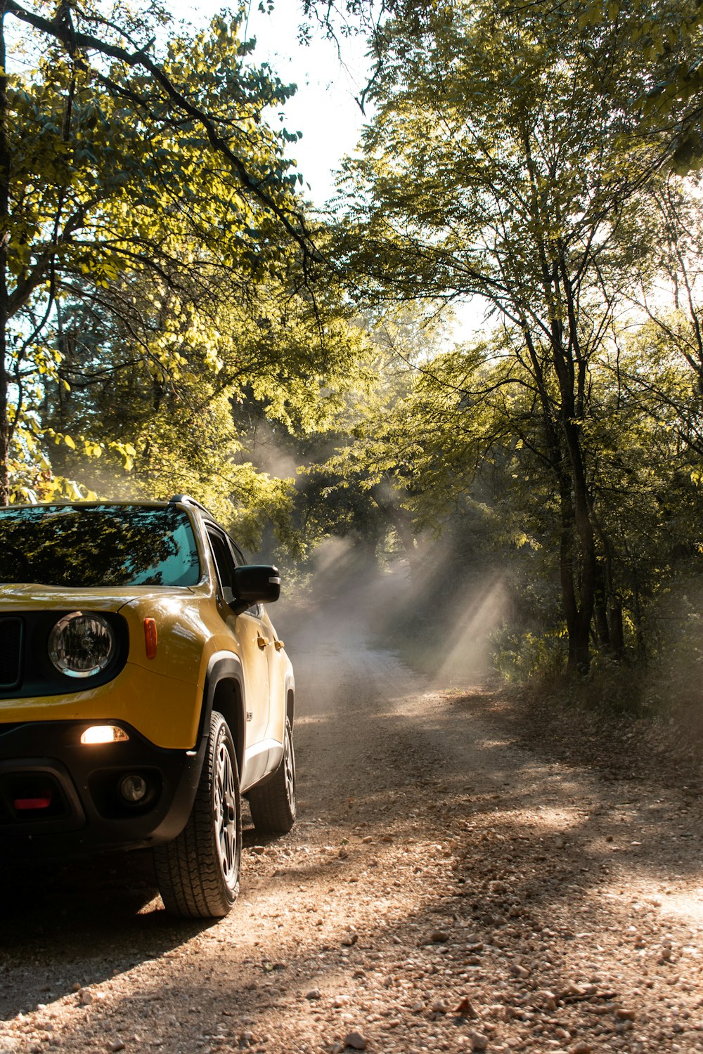 a yellow car on a dirt road with trees on either side of it