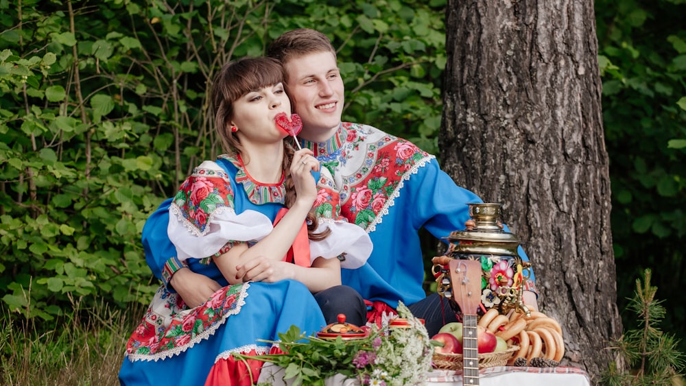 a man and woman sitting next to a tree and eating