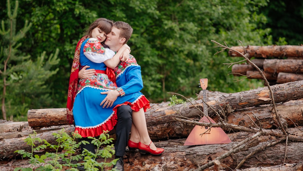 a man and woman sitting on a log in the woods